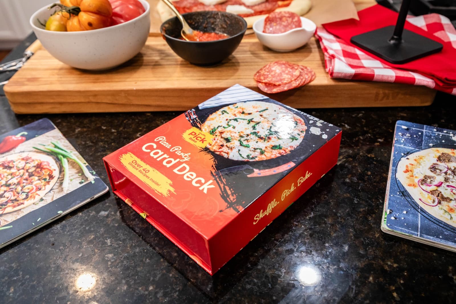 Pizza Party Card Deck packaging on a kitchen counter beside a fresh pizza and topping ingredients